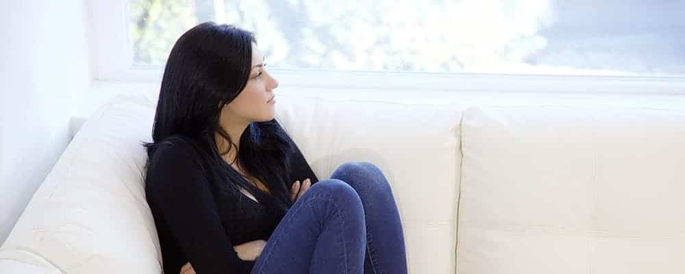 Woman suffering from domestic violence sitting on a couch looking out the window