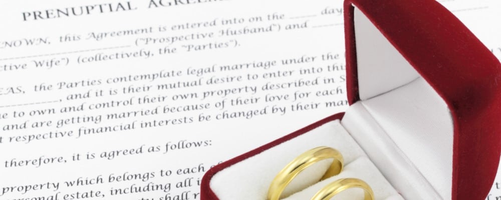 Prenuptial agreement paperwork with a pair of gold rings in a case sitting on top