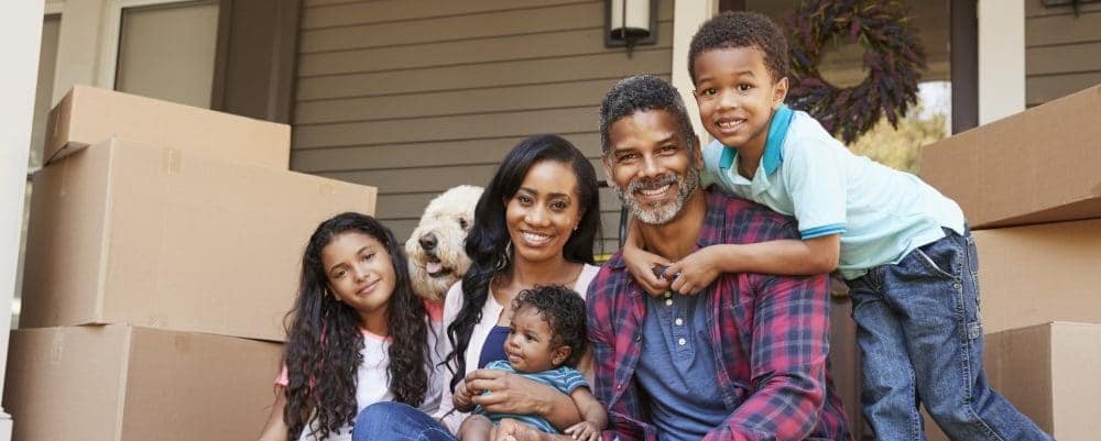 interracial family sitting on their front steps with moving boxes next to them